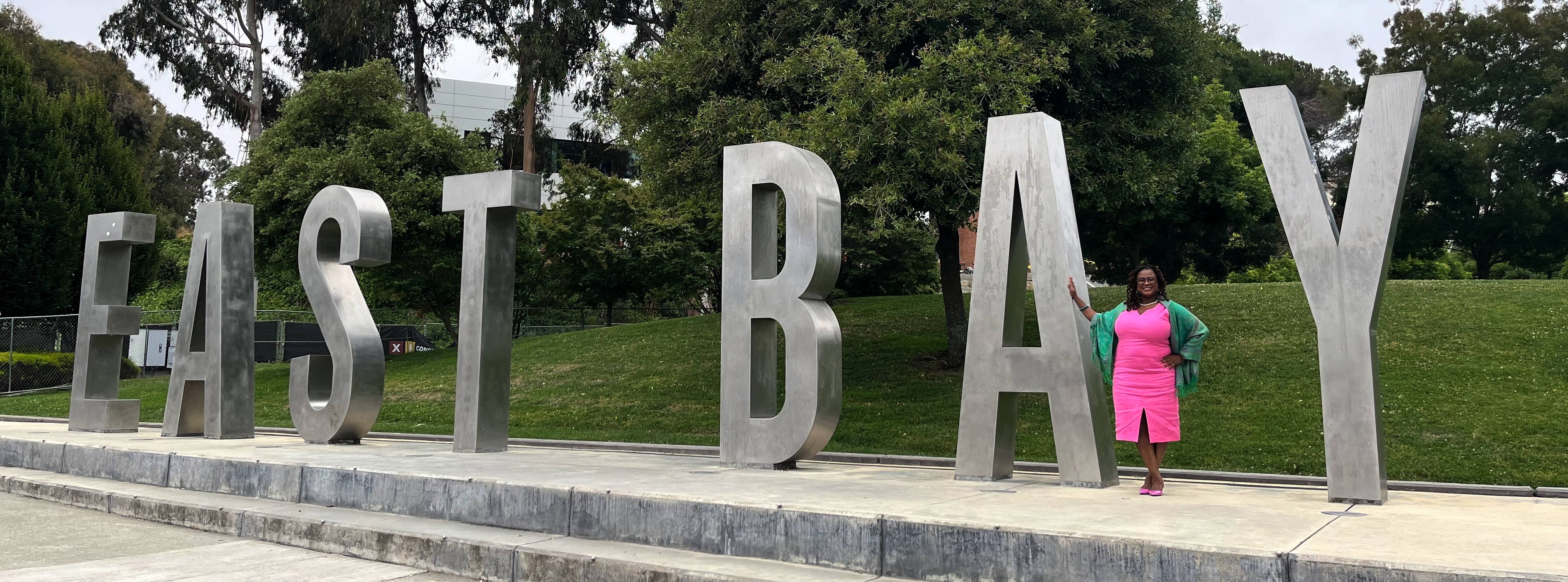 A photograph of Shonda Goward next to a monument sign that reads East Bay